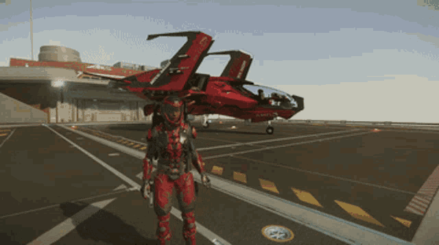 a man in a red suit stands on a runway next to a red jet with the letters tc on the tail