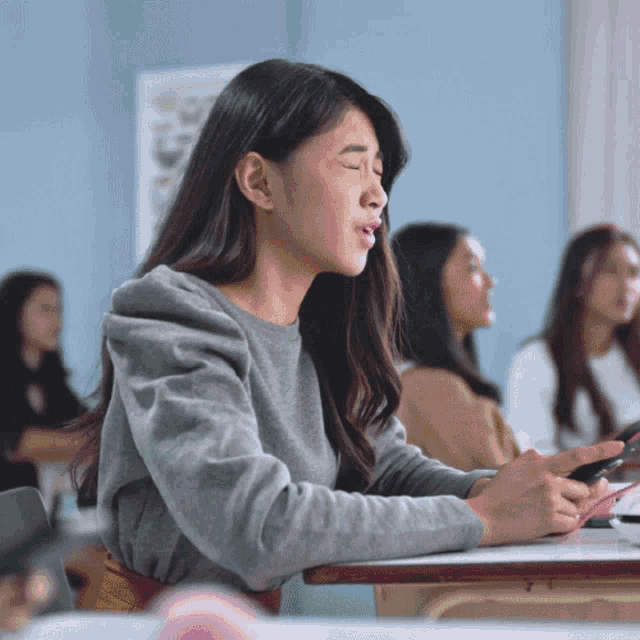 a woman sits at a desk in a classroom with her eyes closed