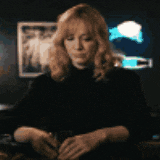 a woman with blonde hair is sitting at a table with her hands folded