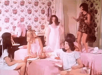a group of women are sitting around a table in a room with pink sheets .