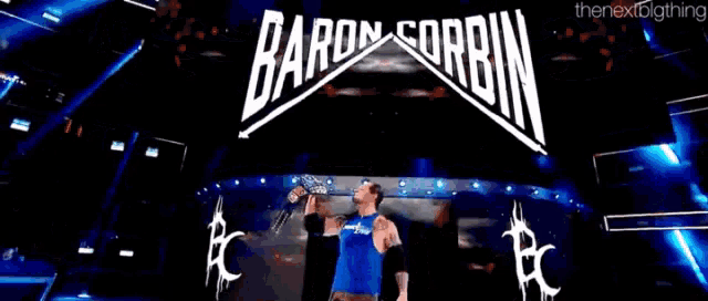 a man in a blue shirt is standing in front of a baron corbin banner