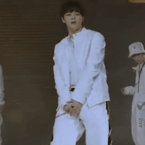 a man in a white suit is dancing on a stage while another man watches .