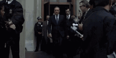 a man in a suit and tie is standing in front of a crowd of reporters and police officers .