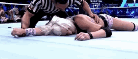 a woman is laying on the floor in a wrestling ring with a referee kneeling over her .