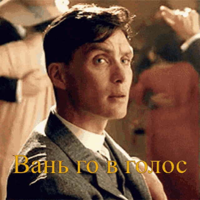 a man in a suit and tie is sitting in front of a sign that says " bath go b tomoc "