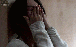 a woman is covering her face with her hands while wearing a sweater .