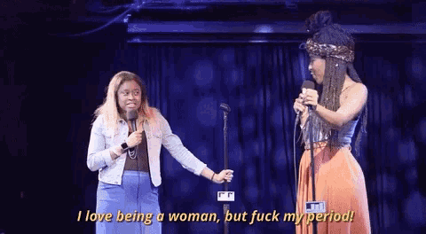 two women on stage with one saying " i love being a woman "