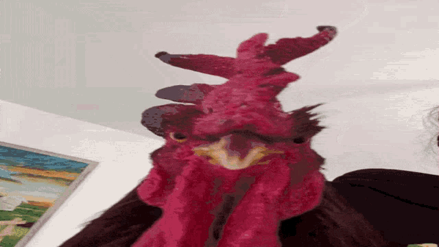 a close up of a red rooster 's head with a painting in the background