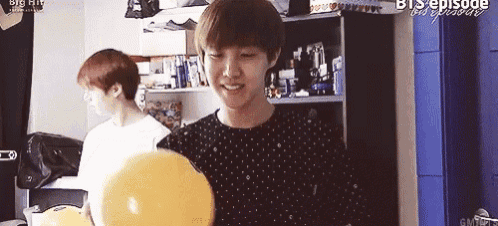 a young man is holding a bowling ball and smiling while another man looks on .