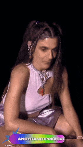 a woman wearing a white tank top and purple shorts sits in front of a banner that says anoytianeprokopos