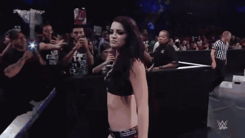 a woman in a black bra stands in front of a crowd with the words # nattyvs paige on the screen