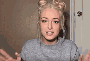 a young woman with blonde hair is wearing a gray sweater and two buns .