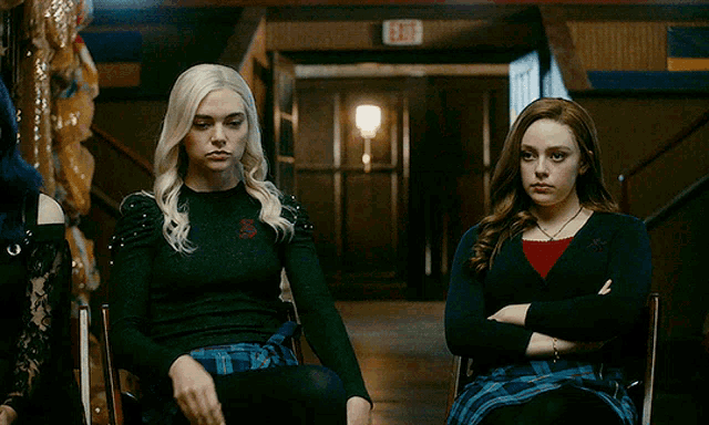two girls are sitting in a hallway with their arms crossed