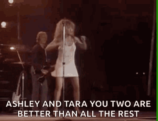 a woman in a white dress is singing into a microphone on stage .