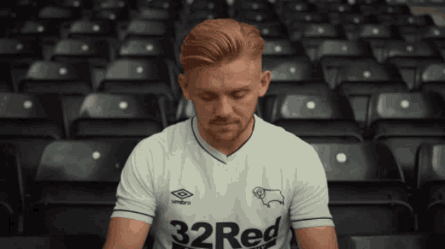 a man wearing a white 32 red shirt sits in a stadium