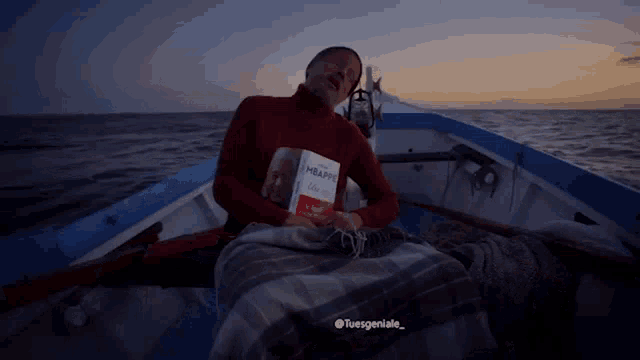 a man sits in a boat holding a book called mbappe