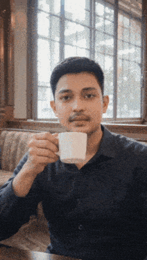a man in a black shirt is drinking from a white mug