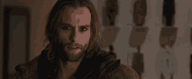 a man with long hair and a beard is standing in a dark room looking at the camera .