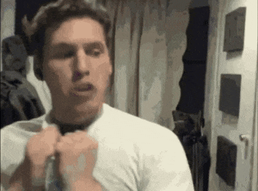 a man in a white shirt is adjusting his tie in front of a mirror in a room .