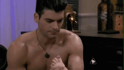 a shirtless man is holding a woman 's foot while sitting on a bed .