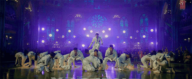 a group of dancers are performing on a stage with purple lights behind them