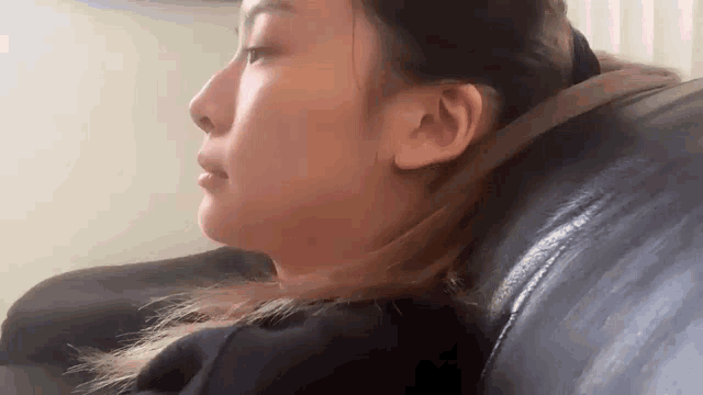 a woman is sitting on a black leather couch with her head resting on the back of the couch .