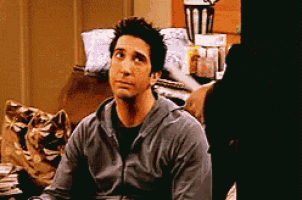 a man in a grey sweatshirt is sitting on a couch looking at the camera .