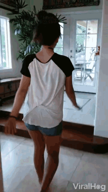 a woman in shorts and a white shirt is dancing in front of a door that says viral hog