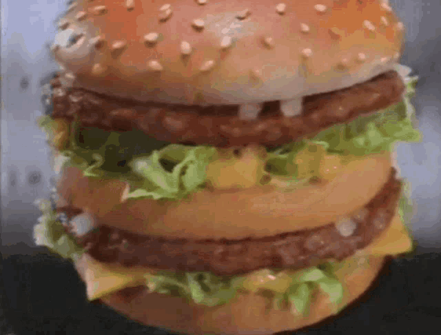 a very large hamburger with lettuce cheese and onions on a bun
