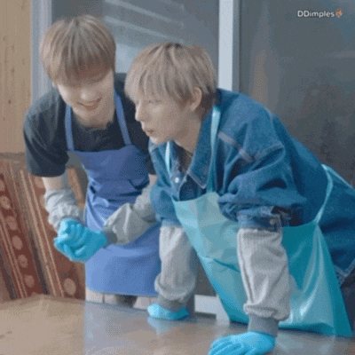two men in blue aprons are cleaning a table with their hands .