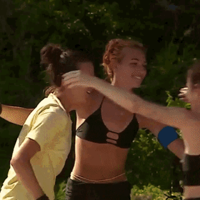 a woman in a black bikini is hugging another woman in a yellow shirt