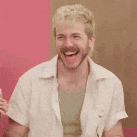 a man with blonde hair and a beard is laughing and waving his hands .