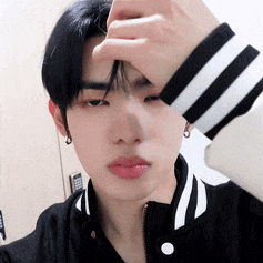 a young man in a black and white striped jacket is covering his face with his hand .