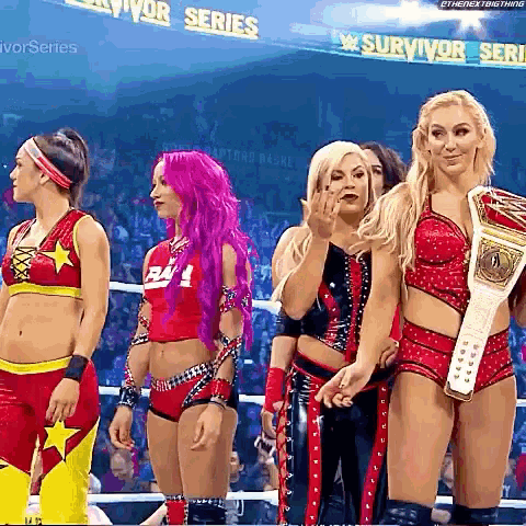 a group of female wrestlers are standing in a ring and one of them is holding a championship belt .
