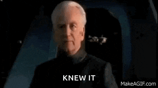 a man in a black suit is standing in a dark room with the words `` knew it '' written on the screen .