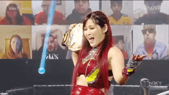 a female wrestler is holding a wrestling championship belt in front of a crowd .