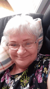 an older woman wearing glasses and a floral shirt is laying on a couch