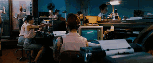 a woman sits at a desk in front of a computer with the letter b on the screen
