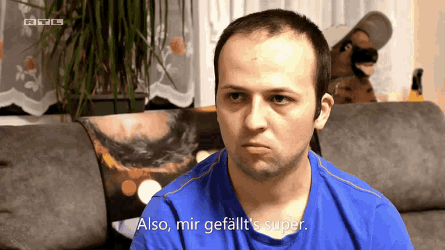 a man in a blue shirt is sitting on a couch and says also mir gefallt 's super
