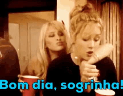 two women are standing next to each other holding red cups and a sign that says bom dia sogrinha .
