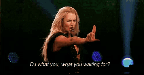 a woman is standing on a stage with a microphone and says dj what you , what you waiting for .