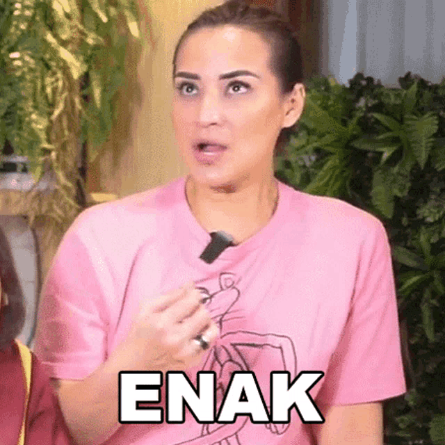 a woman in a pink t-shirt is holding a piece of food and the word enak is on her shirt .