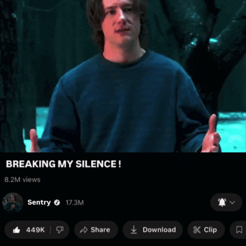 a man in a blue sweater is standing in front of a tree and says breaking my silence