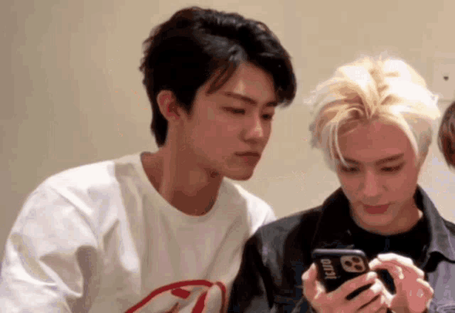 two young men are looking at a cell phone together . one of the men is wearing a black jacket .