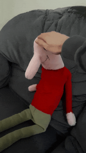 a stuffed animal with a red shirt and green pants is laying on a grey couch
