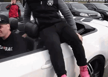 a man wearing a raiders jacket is sitting on the side of a car .