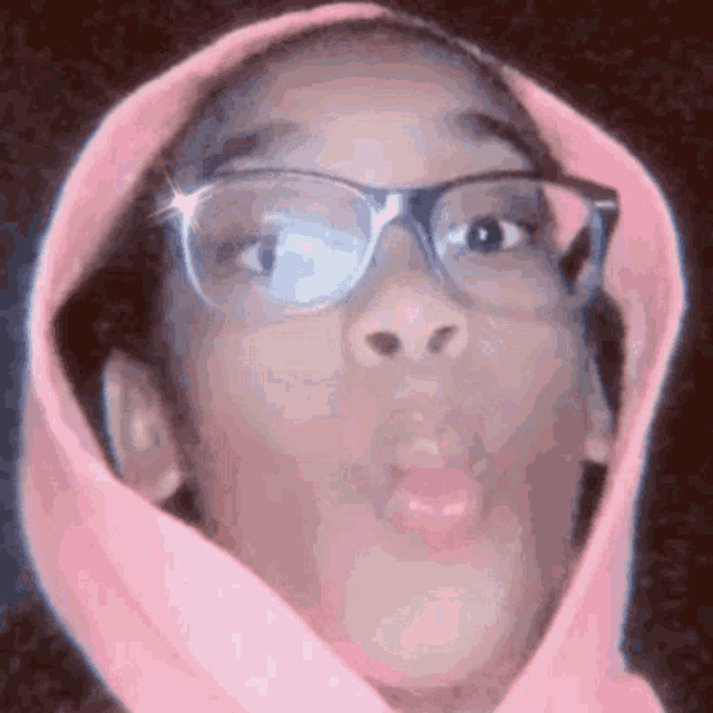 the girl is wearing glasses and a pink hoodie and making a funny face .