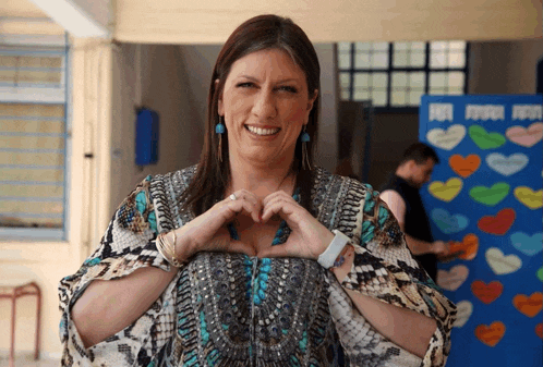 a woman making a heart shape with her hands in front of a wall with hearts