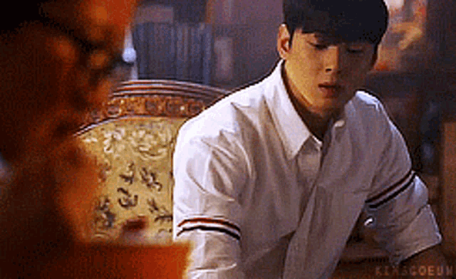 a man in a white shirt is sitting at a table looking at another man .
