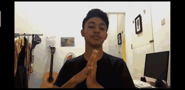a man with his hands folded in front of a guitar and a computer
